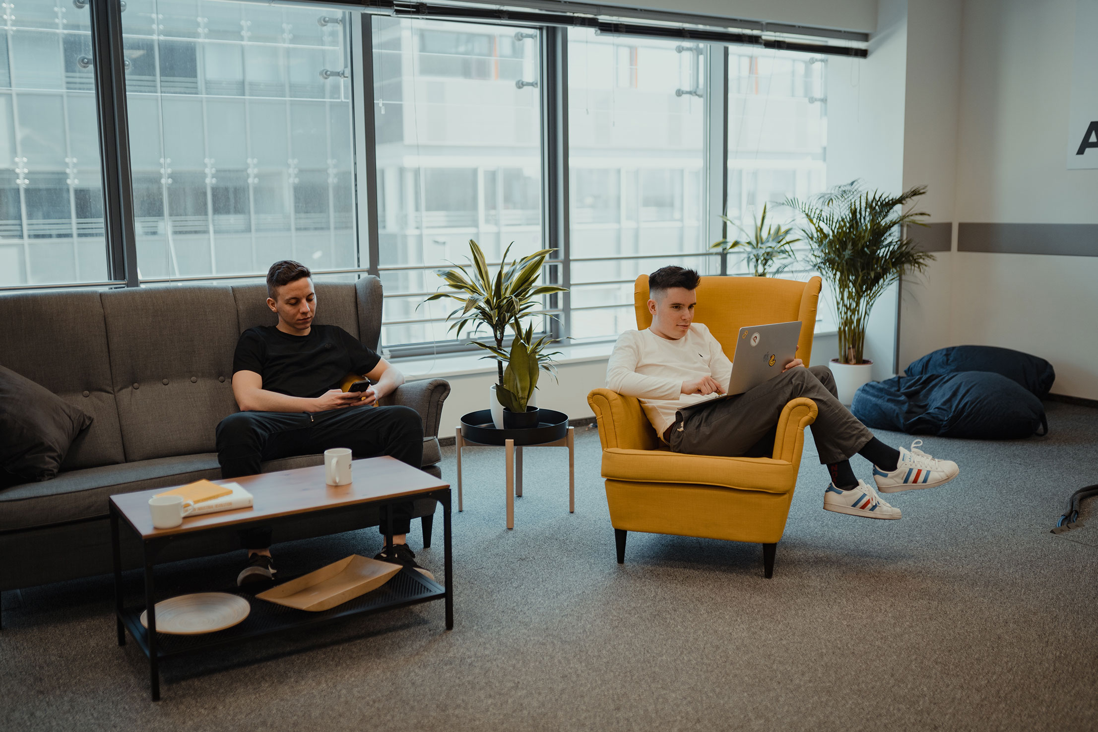 Two people working, one sitting on a couch, the other one on a chair next to it