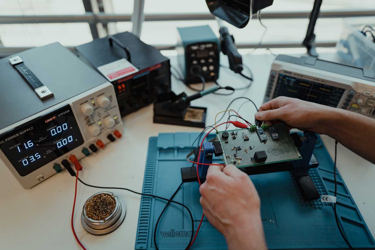 A prototype board connected to a power supply. Two hands reaching from the side, tweaking some components