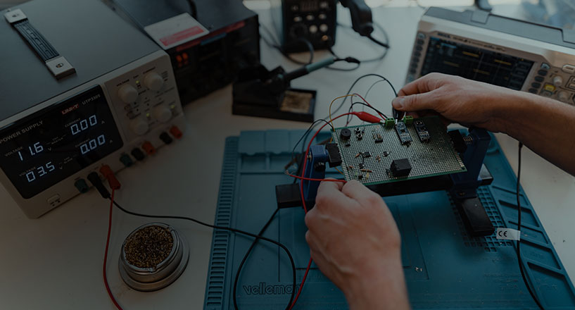 A prototype board connected to a power supply. Two hands reaching from the side, tweaking some components