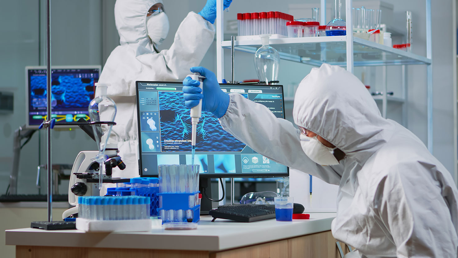 A scientist in a protective overall and a mask, dispensing a liquid into a flask in a lab